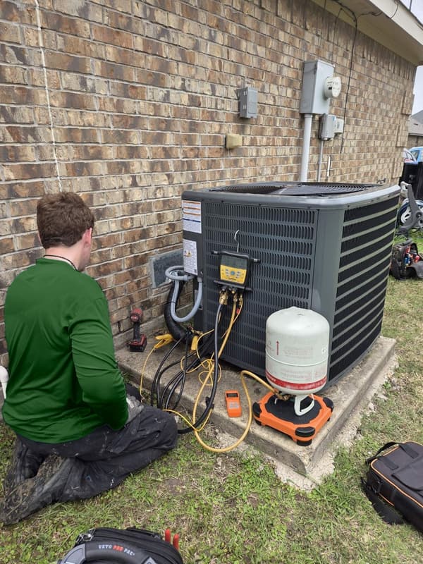 Forefront tech checking a condenser with digital manifold gauges and a refrigerant tank on a scale